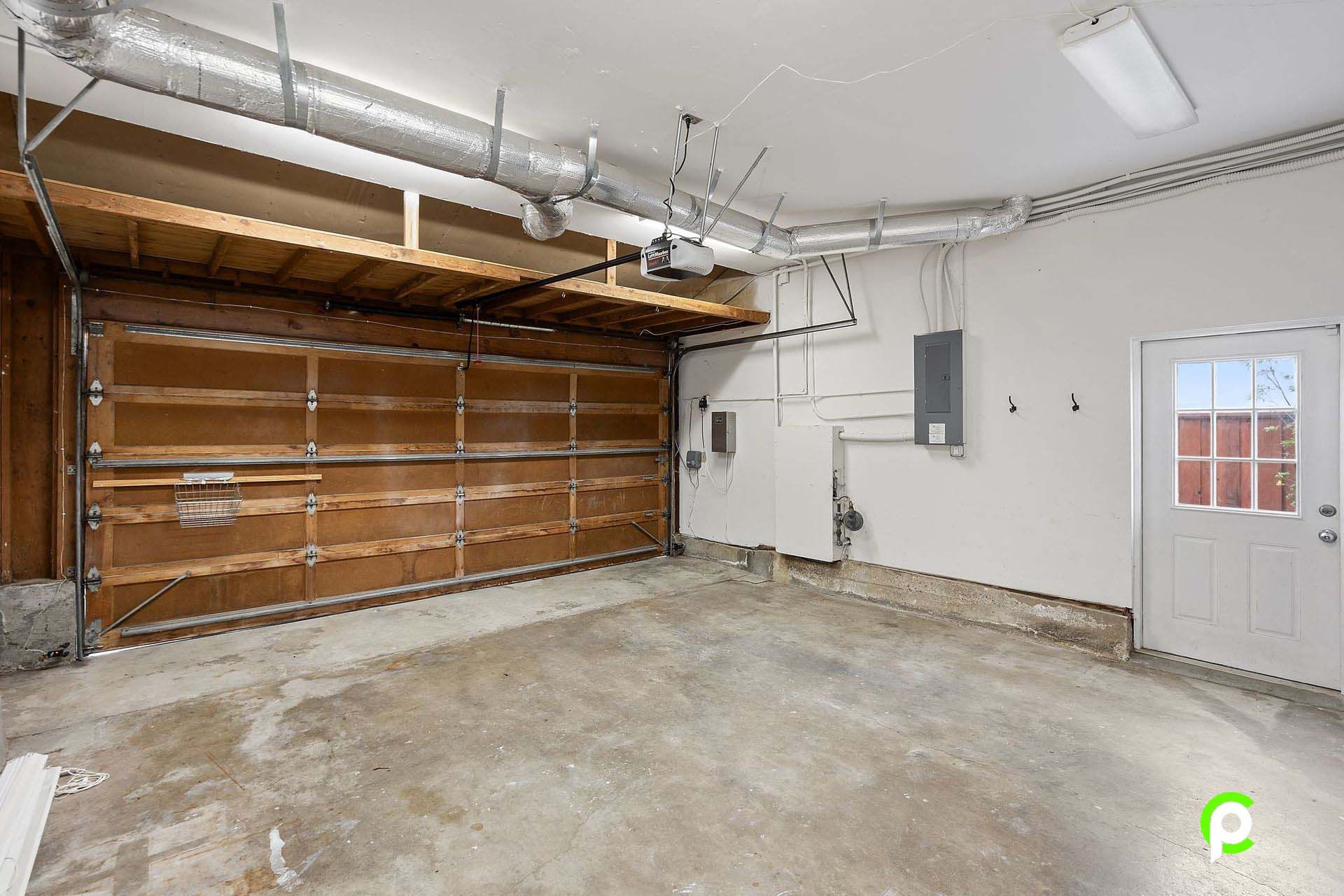 An empty garage with a wooden garage door and a white door.