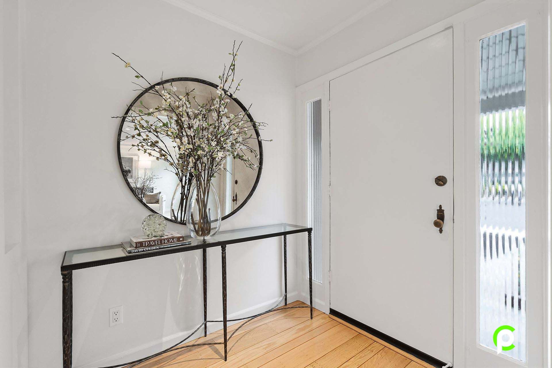 A hallway with a table , mirror and vase of flowers.