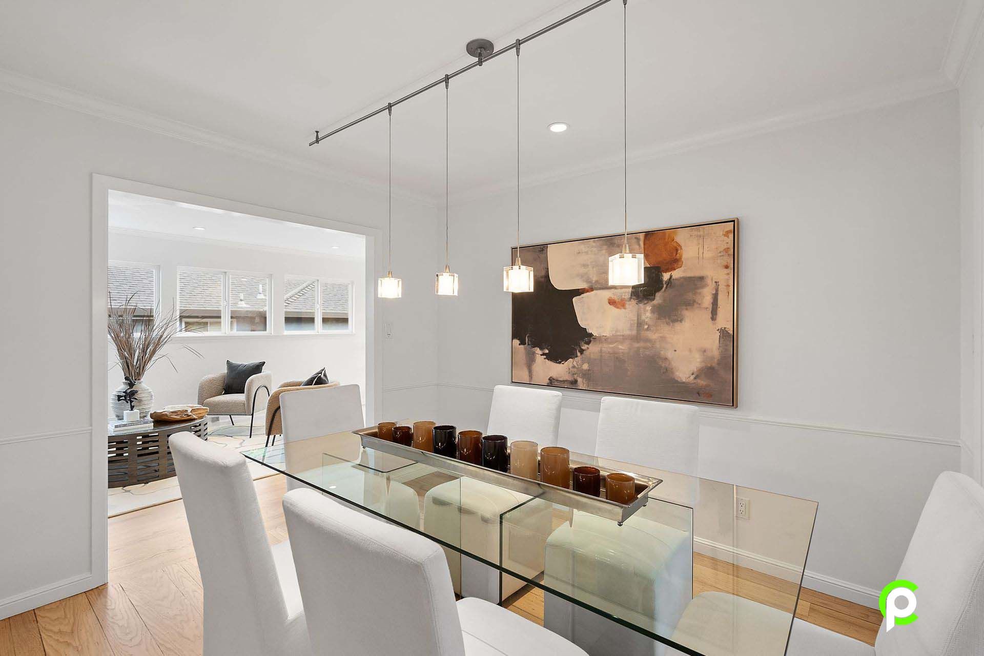 A dining room with a glass table and chairs and a painting on the wall.