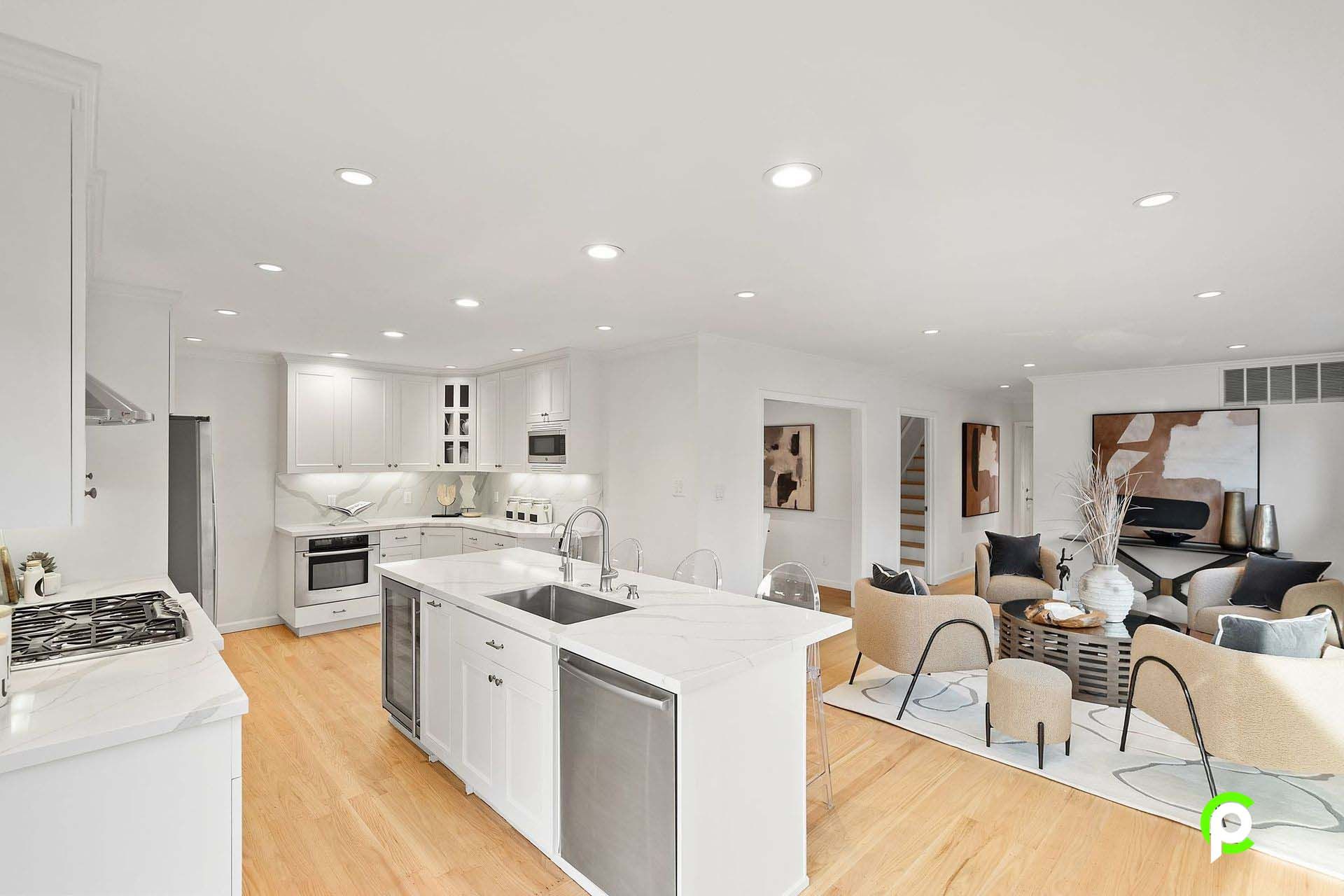 A kitchen with white cabinets and stainless steel appliances is connected to a living room and dining room.