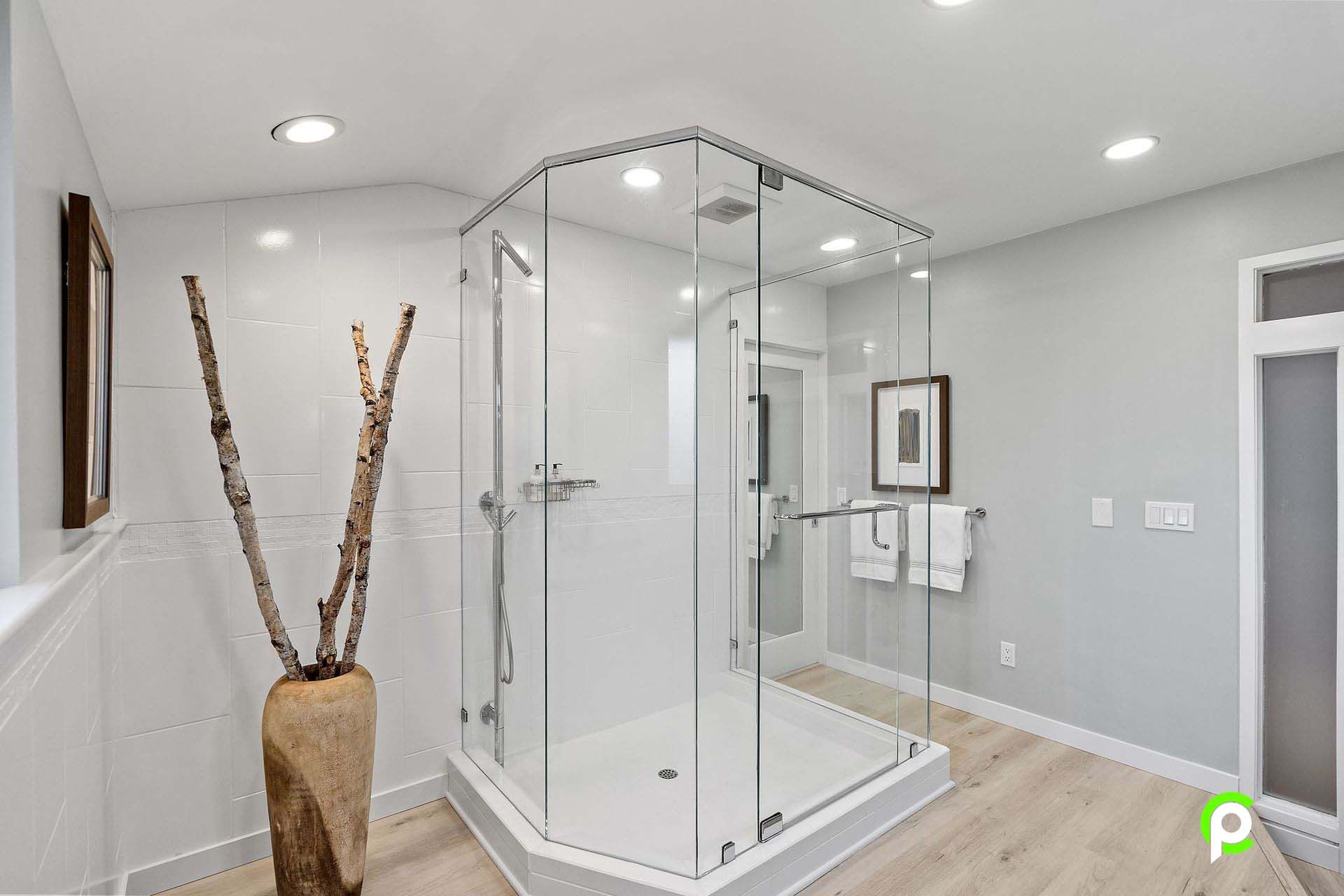 A bathroom with a walk in shower and a vase of branches.