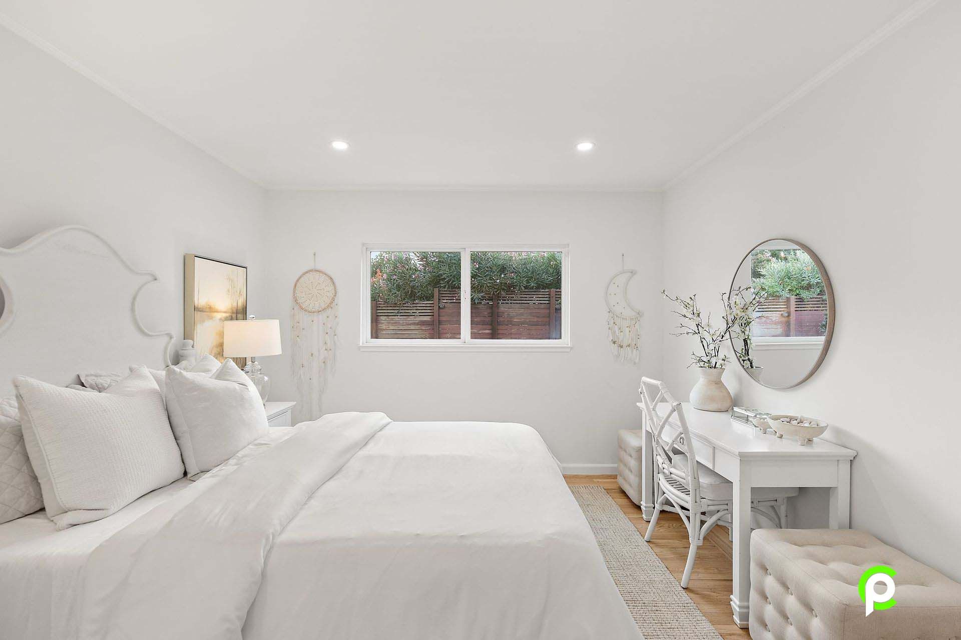 A bedroom with a bed , desk , mirror and two windows.