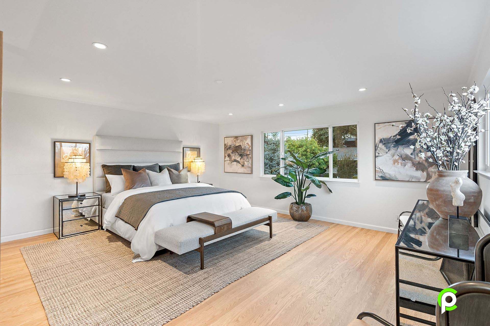 A bedroom with a large bed , a bench , a table and a window.