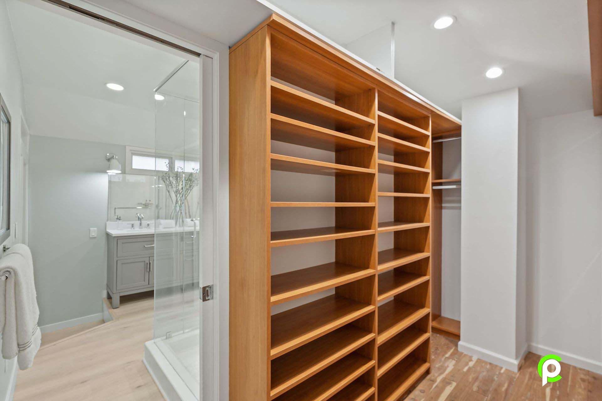 A walk in closet with wooden shelves and a bathroom in the background.