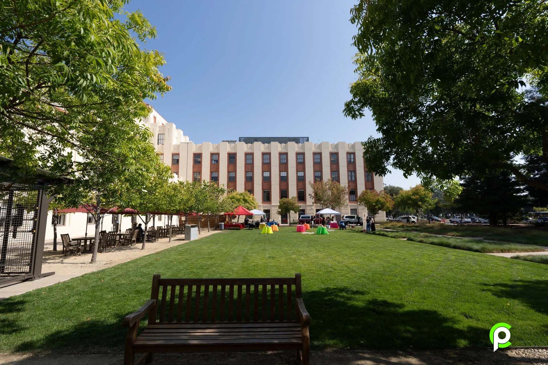 A park with a large building in the background and a bench in the foreground