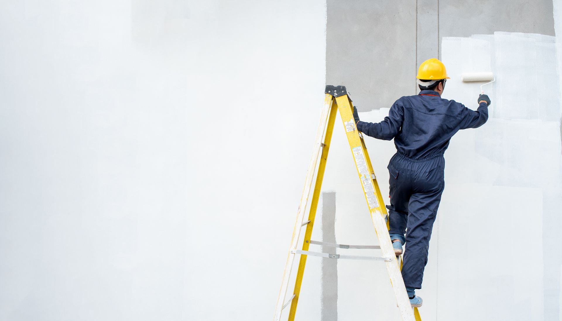 A man is standing on a ladder painting a wall.