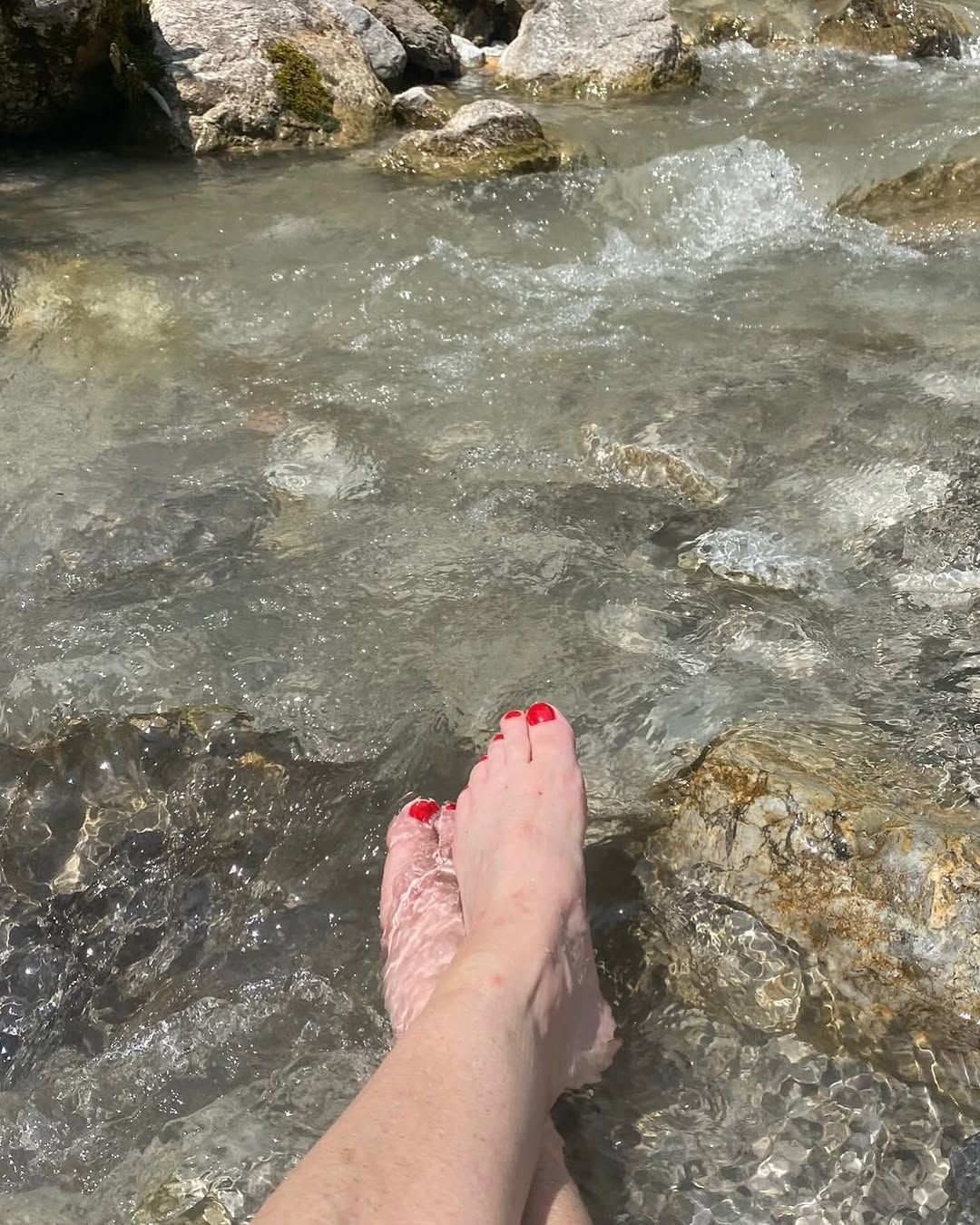 Die Füße einer Frau mit rotem Nagellack sind im Wasser.