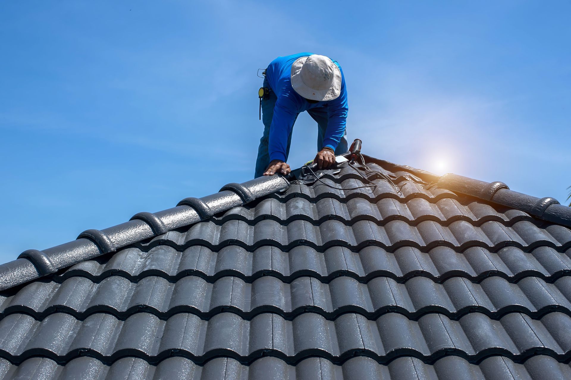 Roofer in Blue Uniform on A Tiled Roof Against a Bright Blue Sky — Newcastle Roofing Wizards In Kurri Kurri, NSW