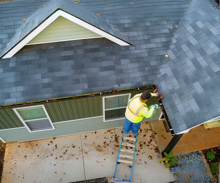 An aerial view of a man on a ladder working on the roof of a house.