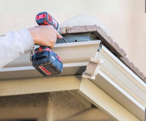 A person is working on a gutter with a cordless drill.