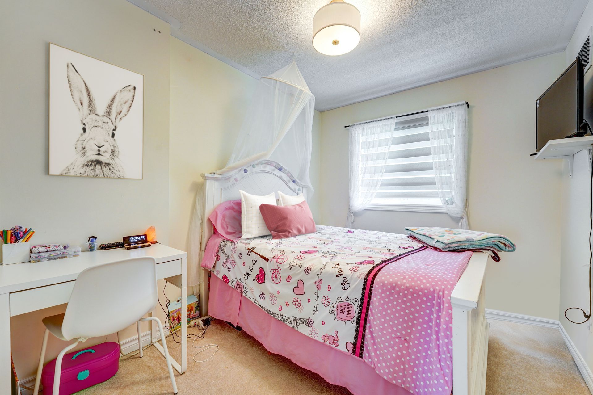 A bedroom with a bed , desk , chair and a picture of a rabbit on the wall.