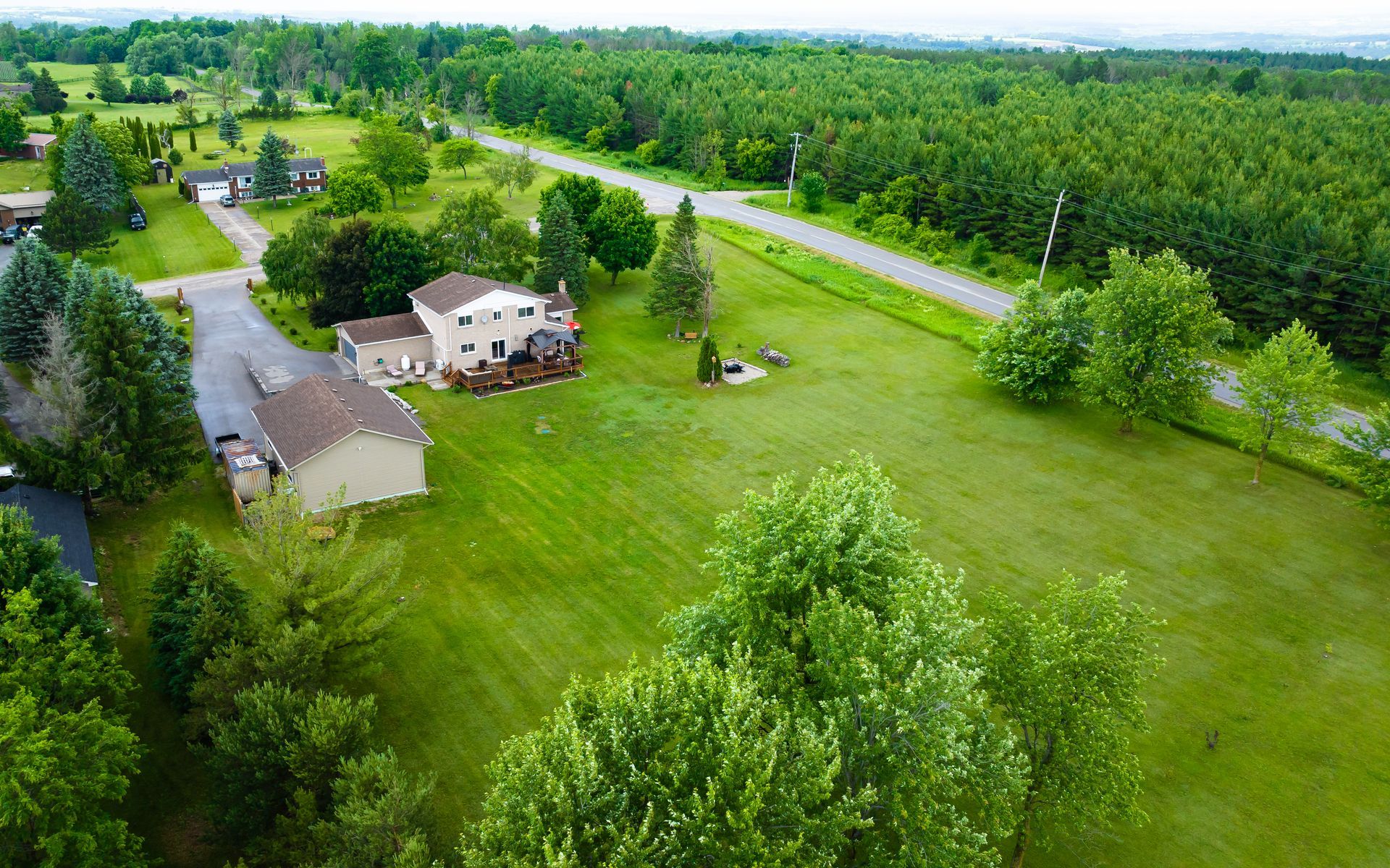 An aerial view of a house in the middle of a lush green field surrounded by trees.