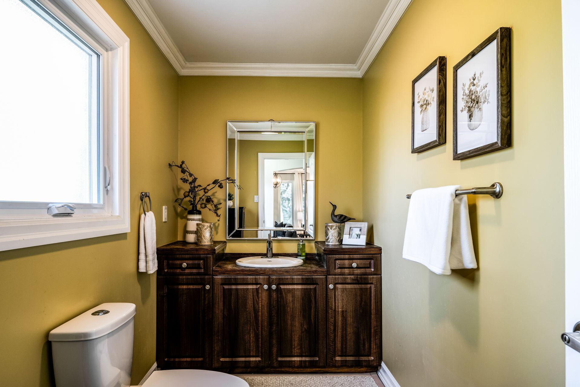 A bathroom with a toilet , sink , mirror and window.
