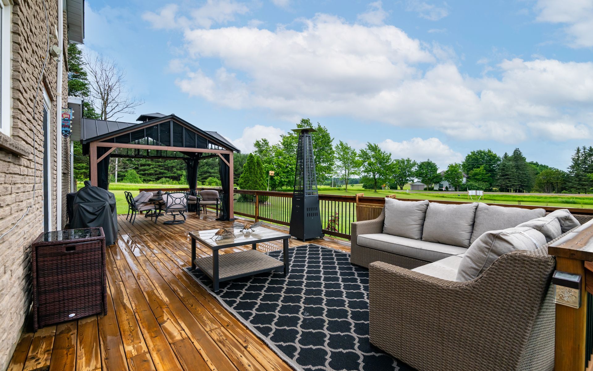 A large wooden deck with a couch , chairs and a gazebo.