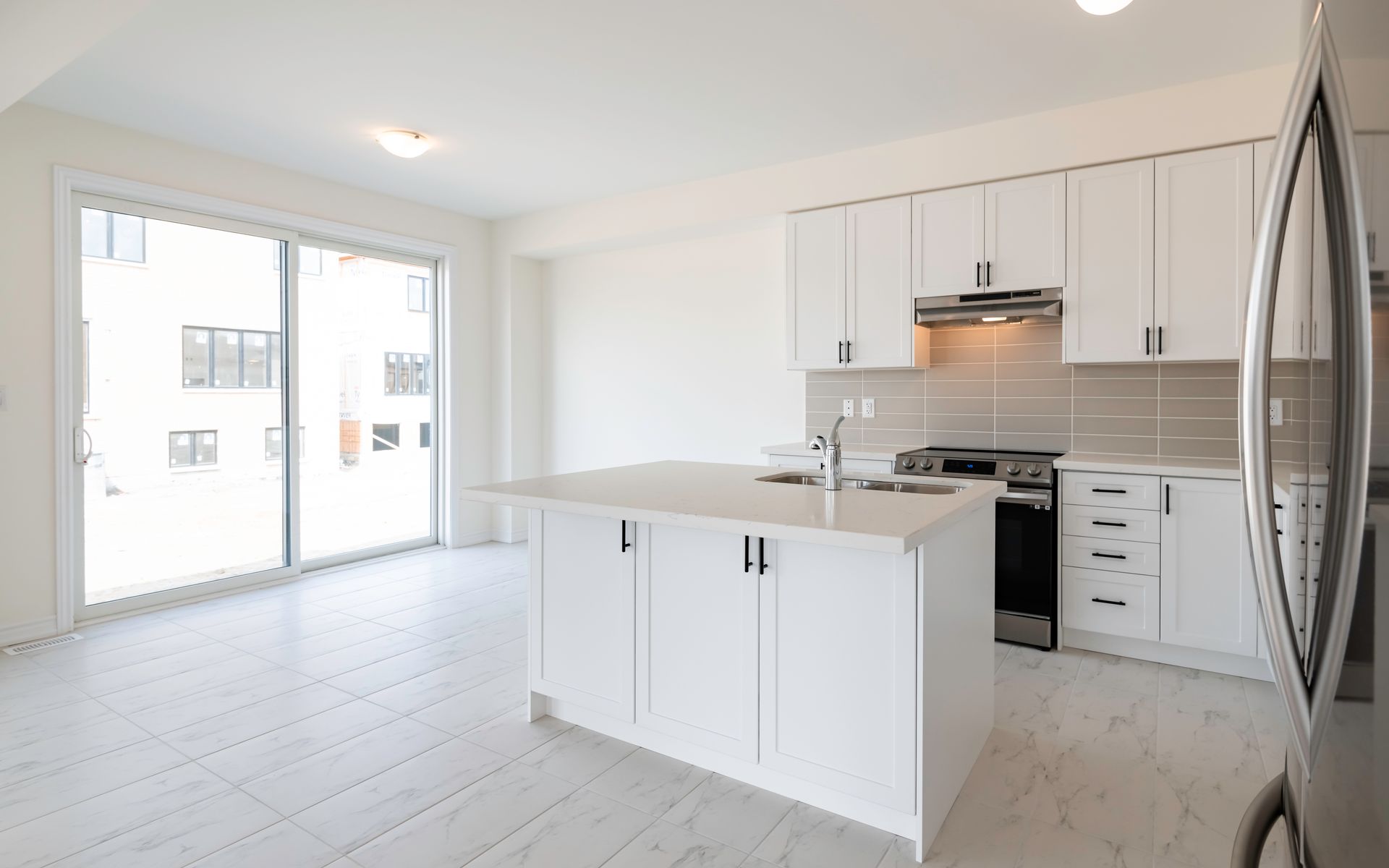 An empty kitchen with white cabinets and stainless steel appliances.