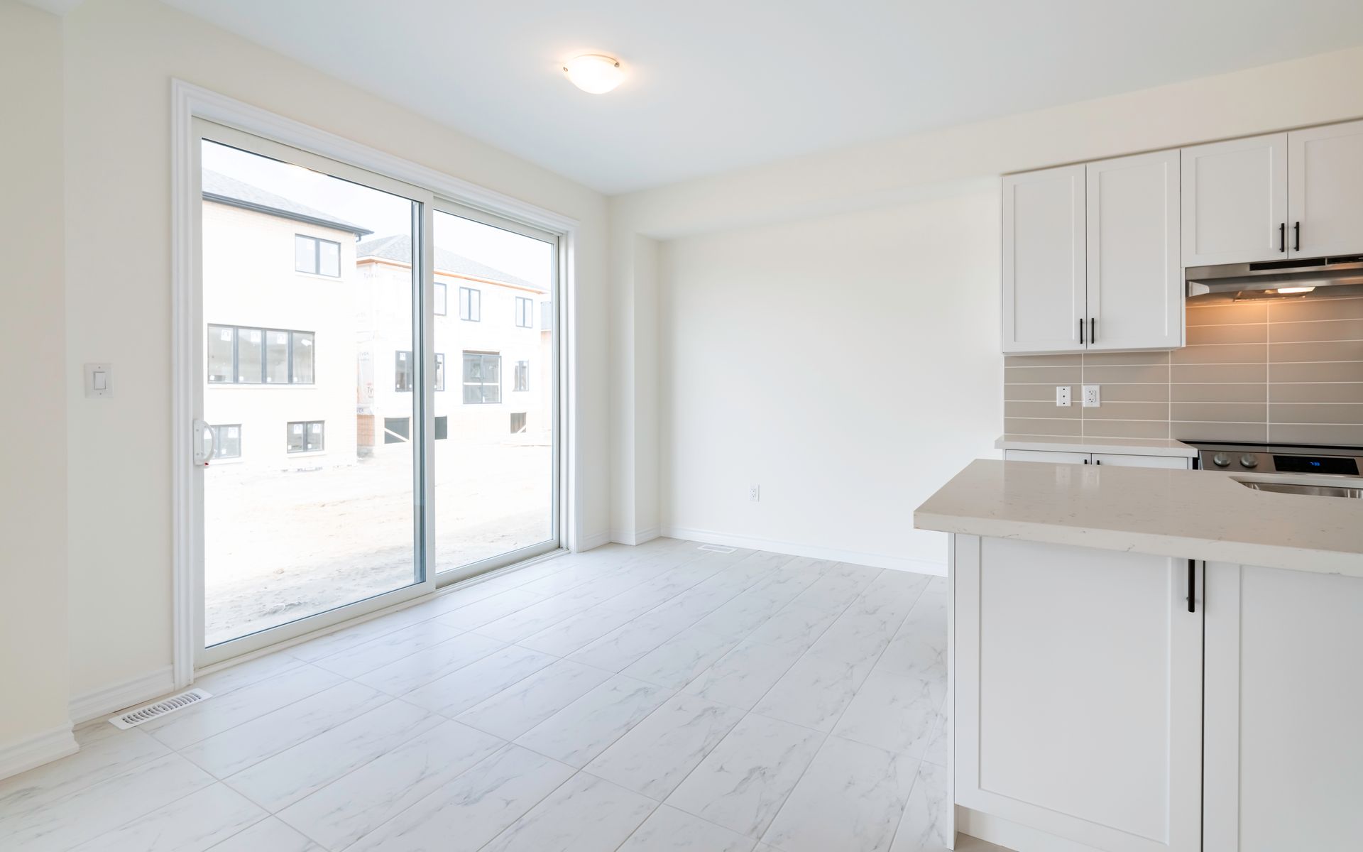 An empty kitchen with white cabinets and sliding glass doors.