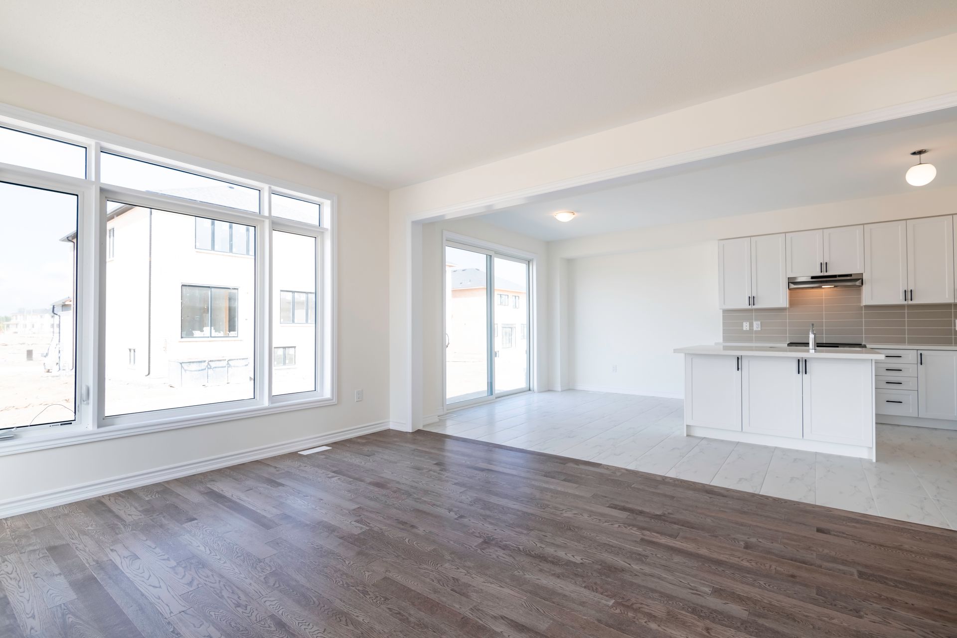 An empty living room with hardwood floors and a kitchen in the background.