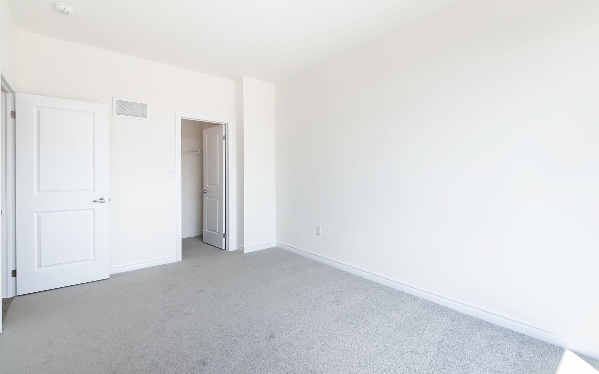 an empty bedroom with a carpeted floor and white walls .