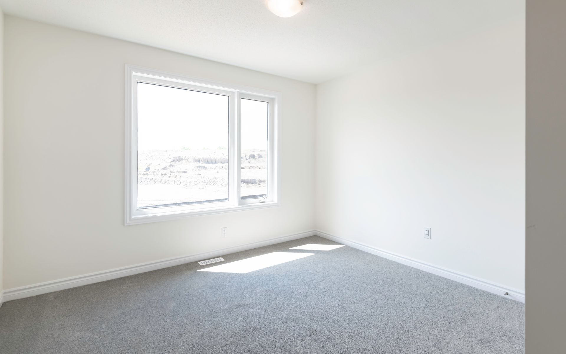 An empty bedroom with a large window and a gray carpet.
