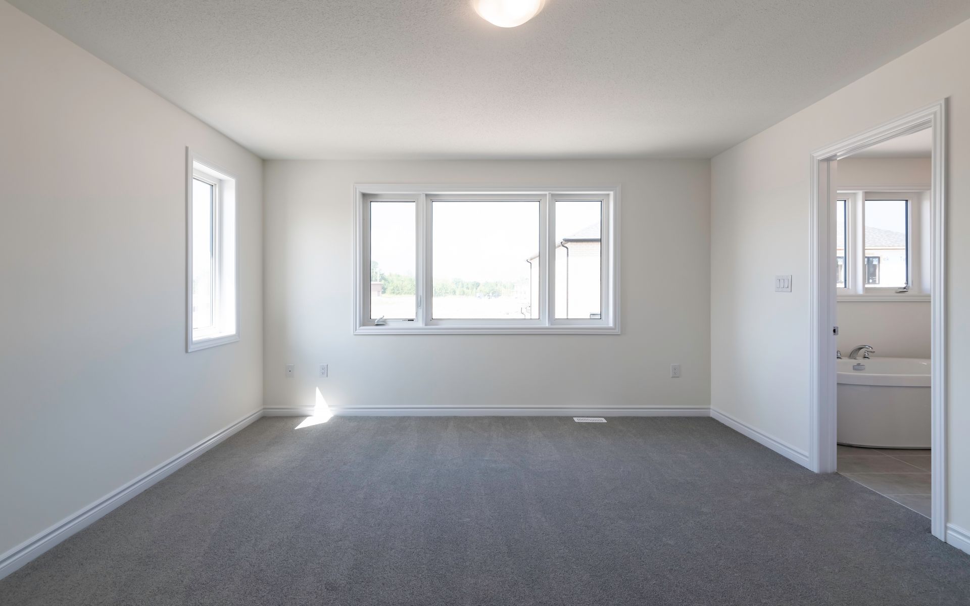 an empty living room with a large window and a gray carpet .