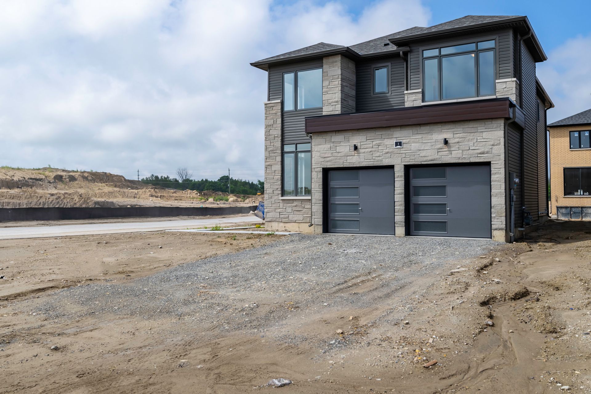 A large house with two garage doors is sitting on top of a dirt field.
