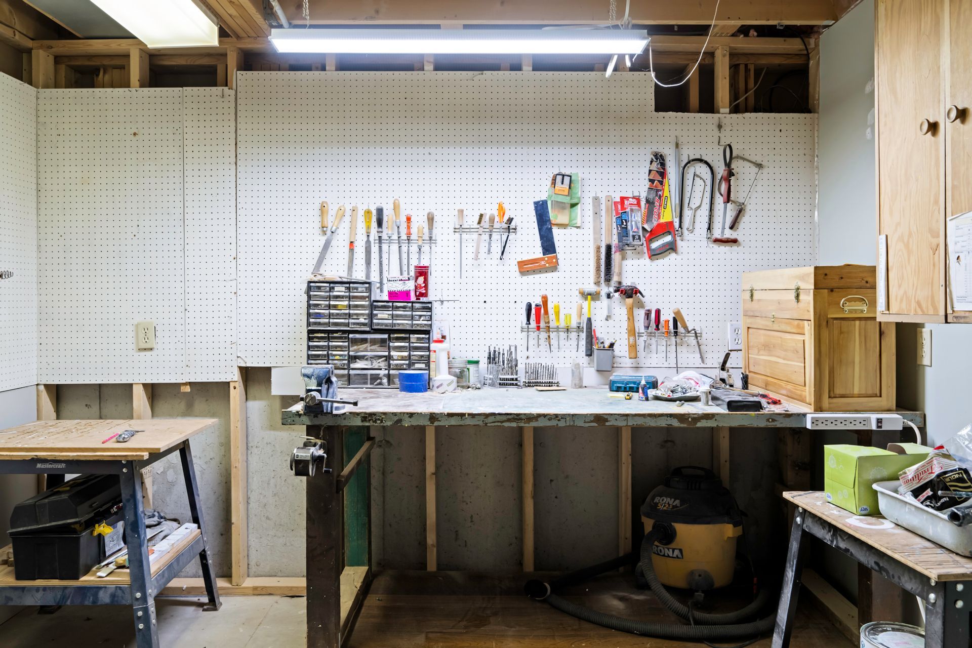 A workbench in a garage filled with tools and a vacuum cleaner.