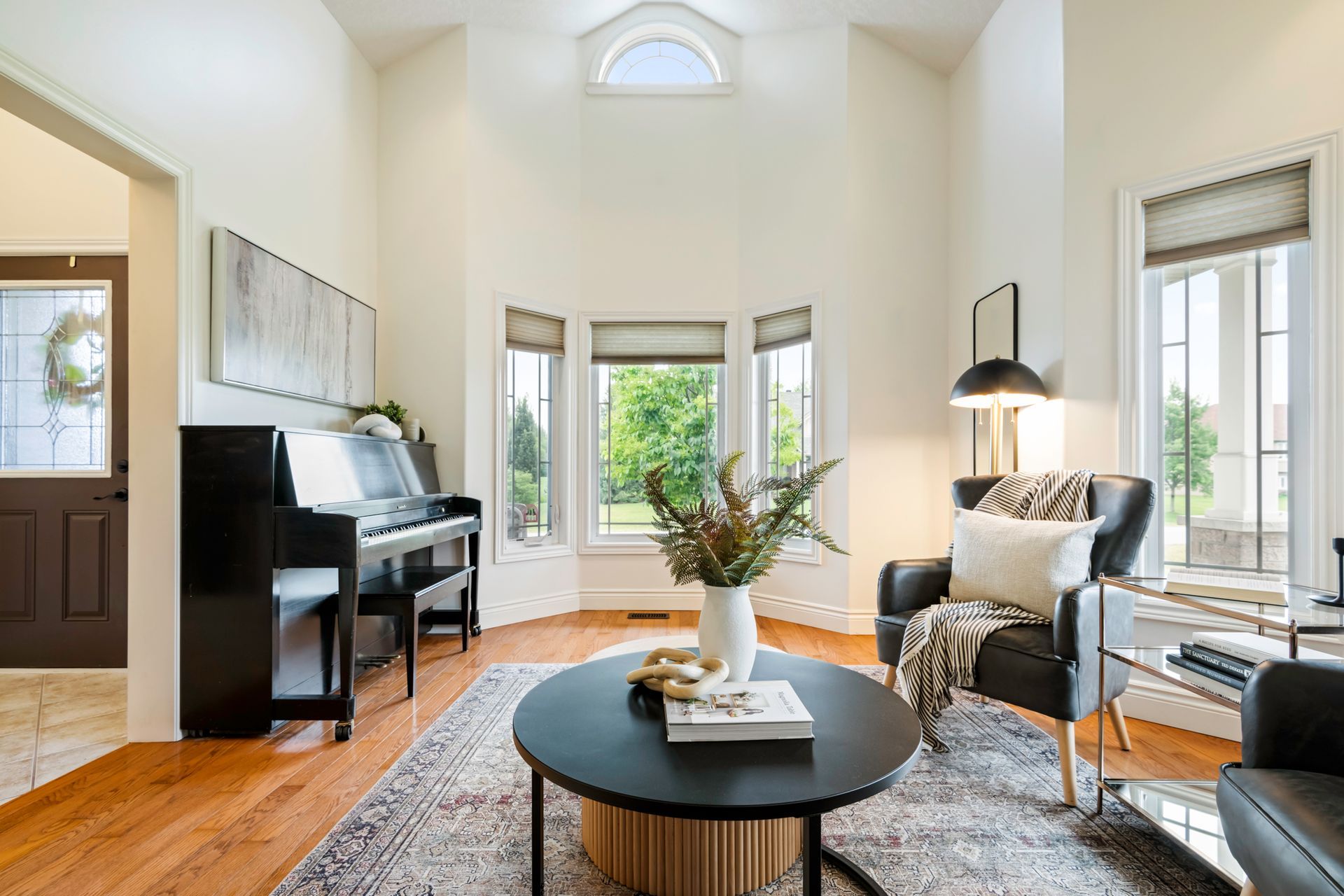 A living room with a piano , chairs , and a round coffee table.