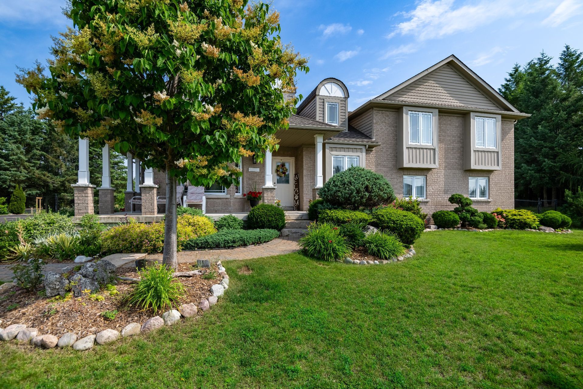 A large brick house with a lush green lawn and a tree in front of it.