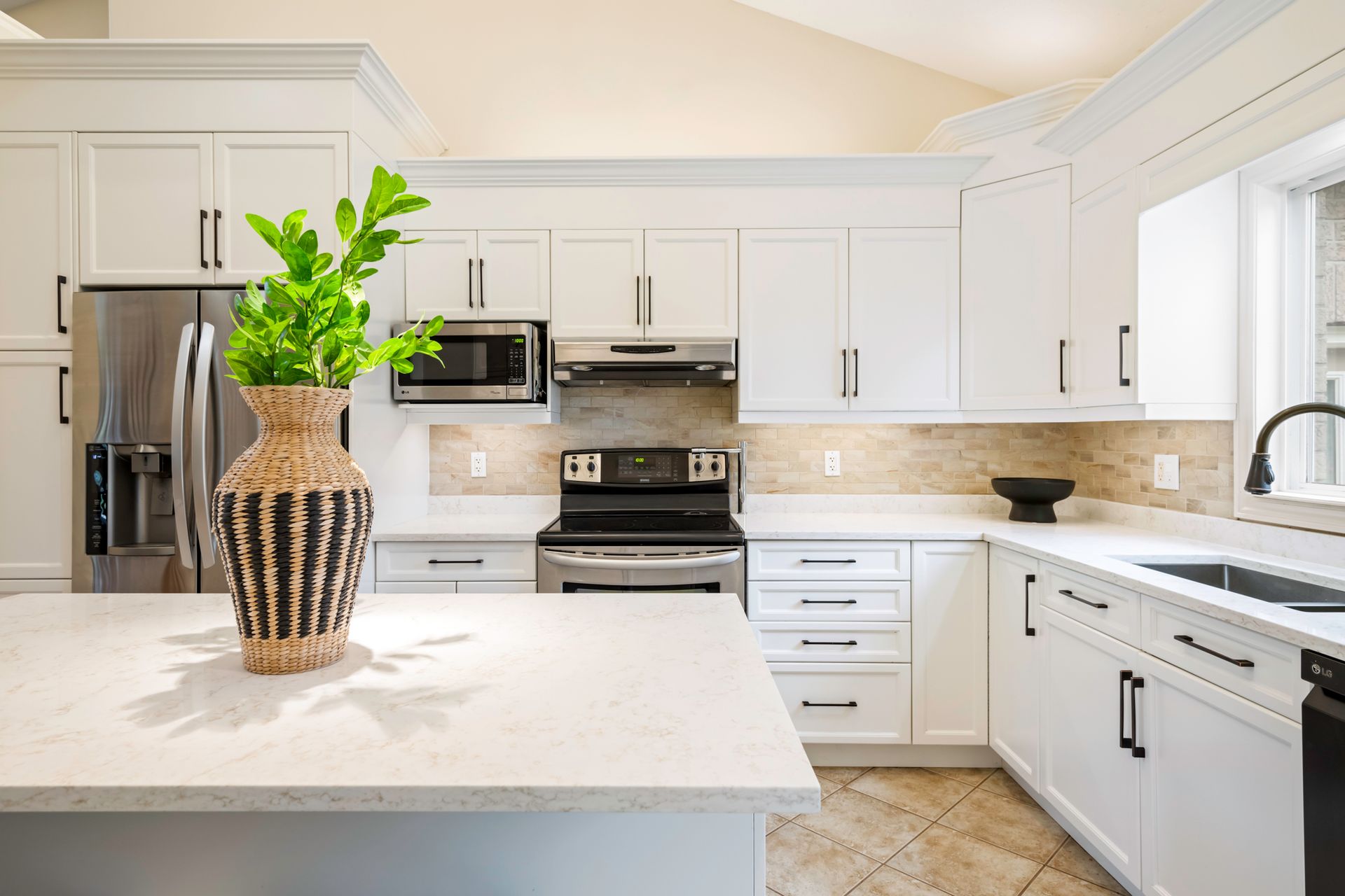 A kitchen with white cabinets , stainless steel appliances , a sink , and a vase on the counter.