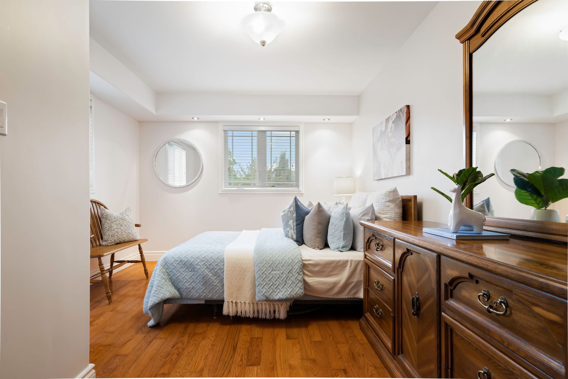 A bedroom with a bed , dresser , mirror and window.