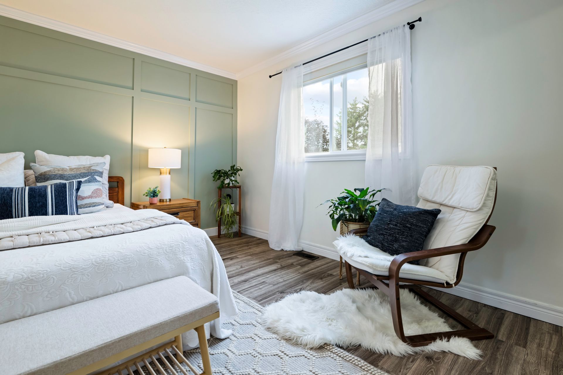 A bedroom with a bed , chair , bench and window.