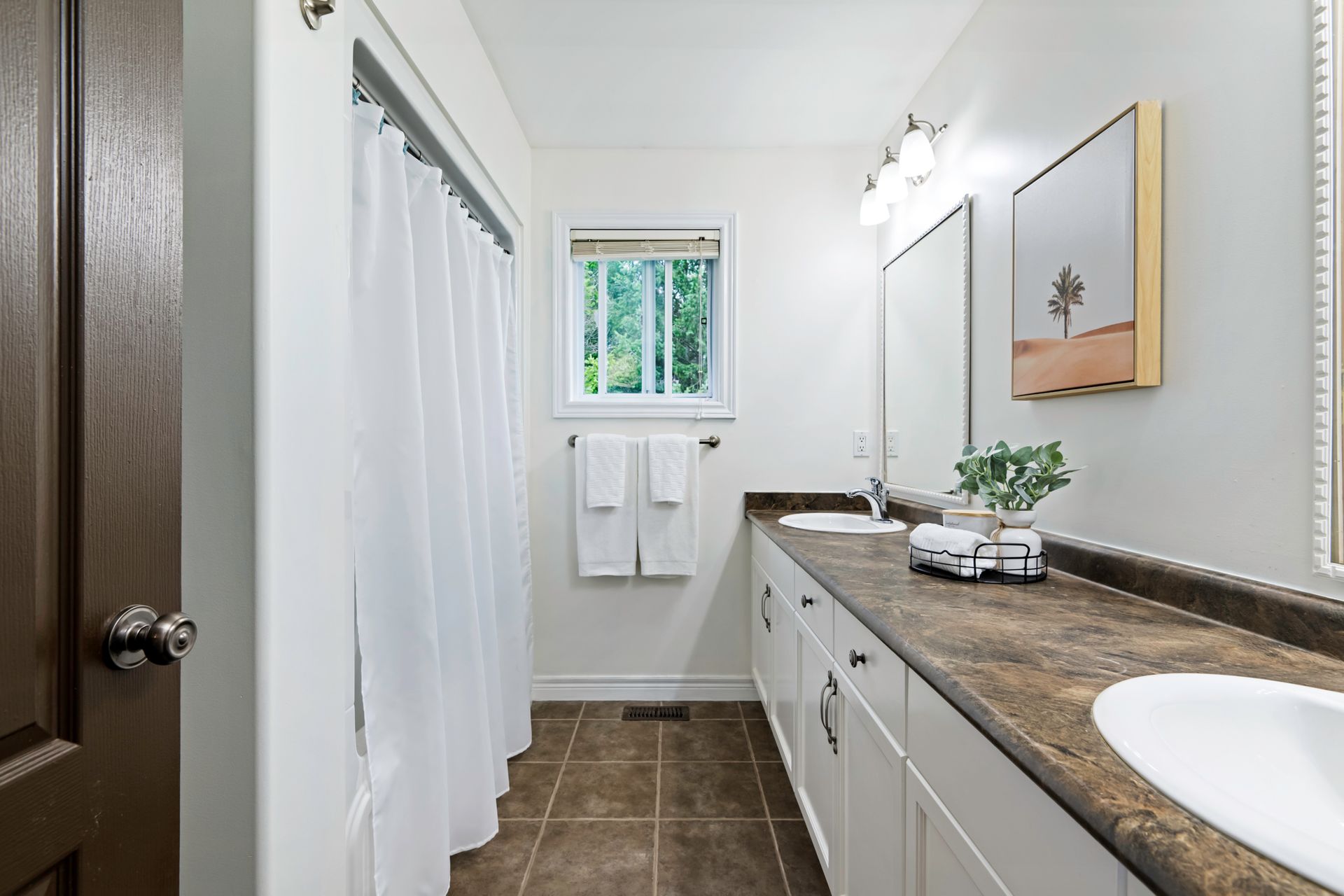 A bathroom with two sinks , a mirror and a window.