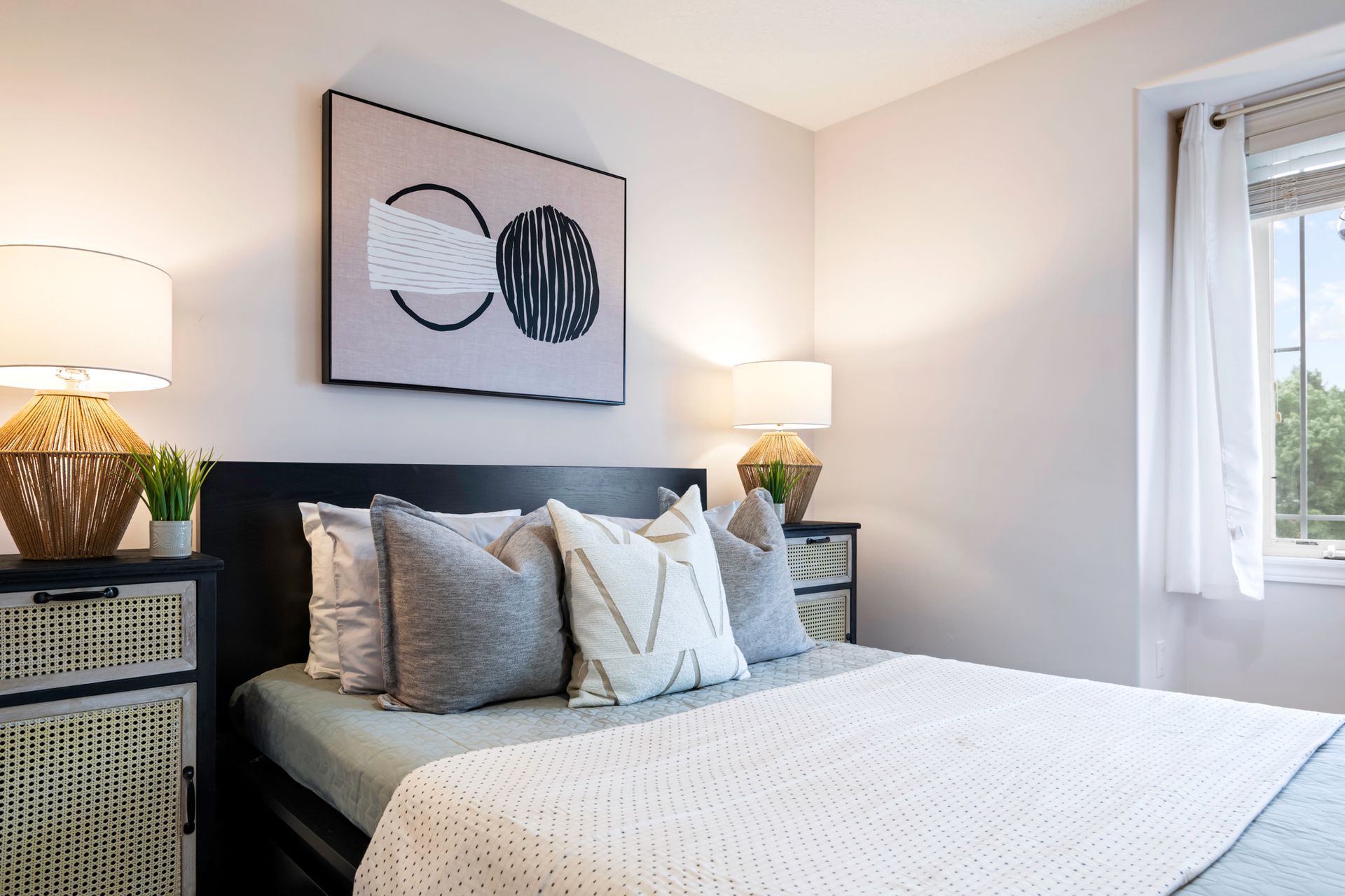 A bedroom with a bed , nightstand , lamps and a painting on the wall above the bed.
