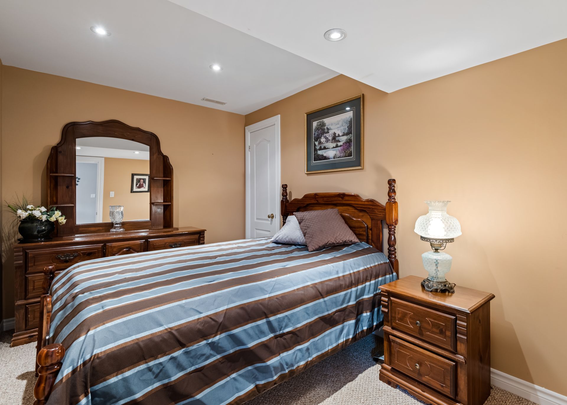 A bedroom with a bed , nightstand , mirror and dresser.