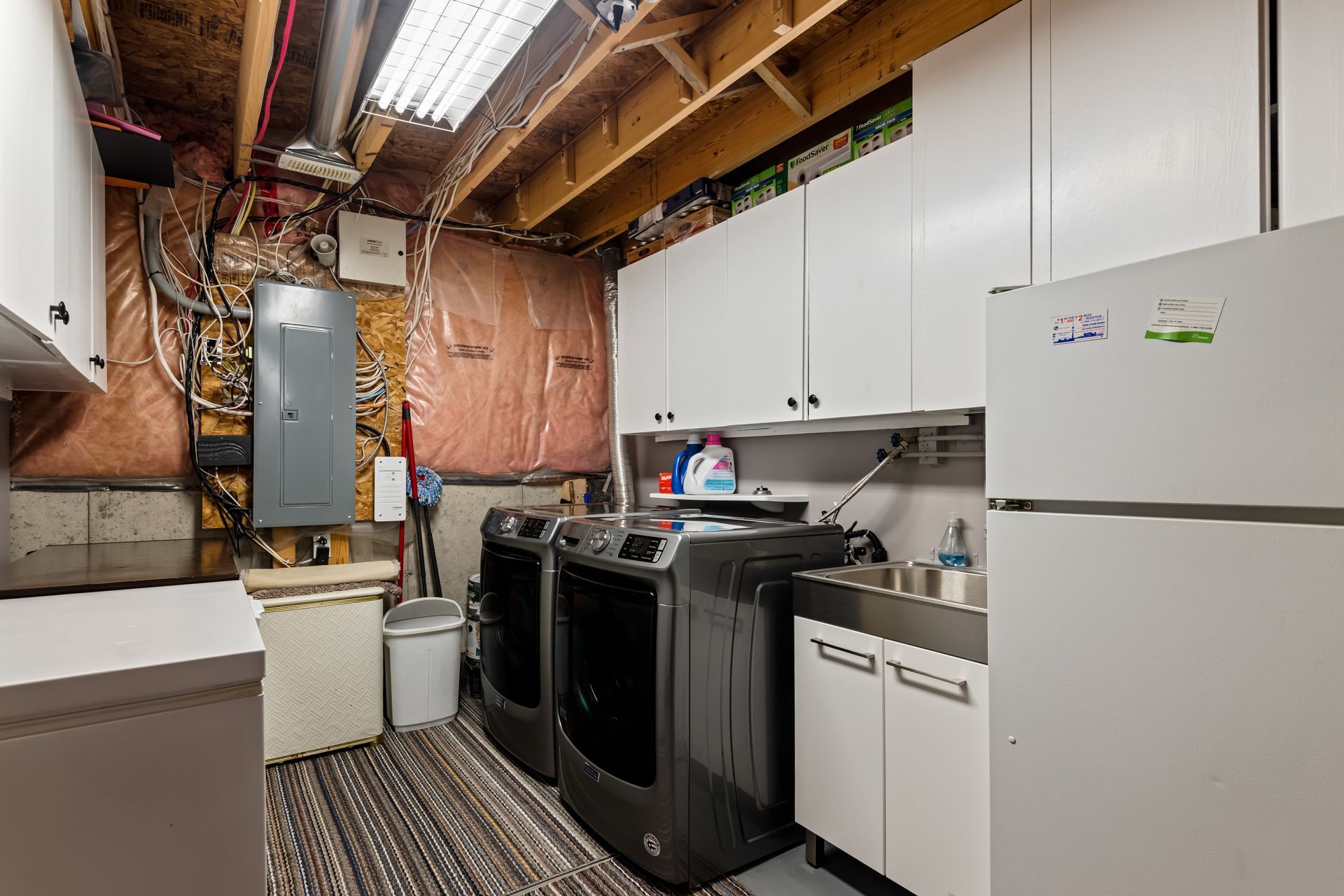 A laundry room with a washer and dryer , refrigerator , sink and cabinets.
