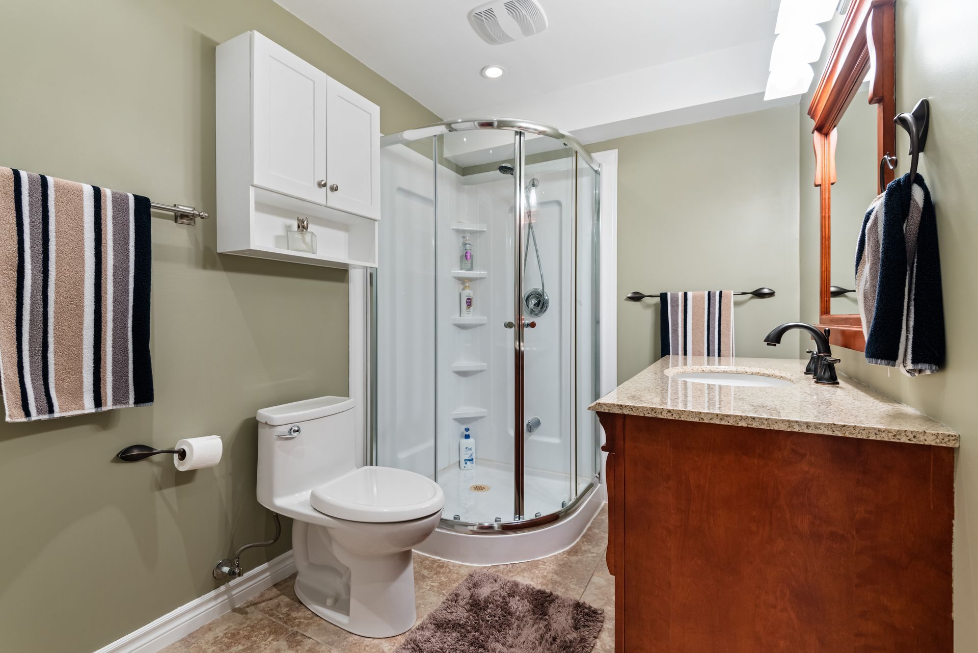 A bathroom with a toilet , sink , shower and mirror.