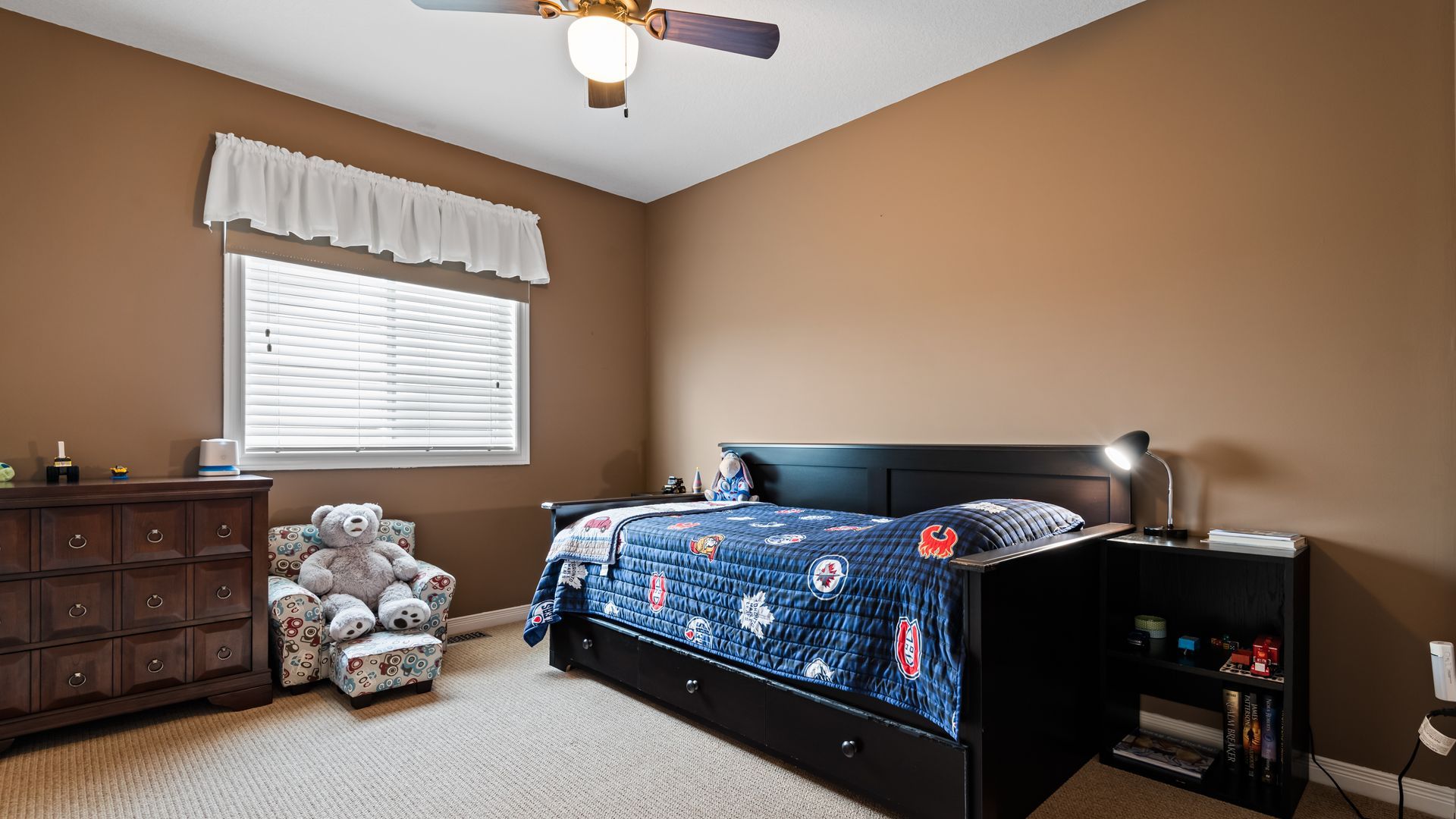 A bedroom with a bed , dresser , chair and ceiling fan.