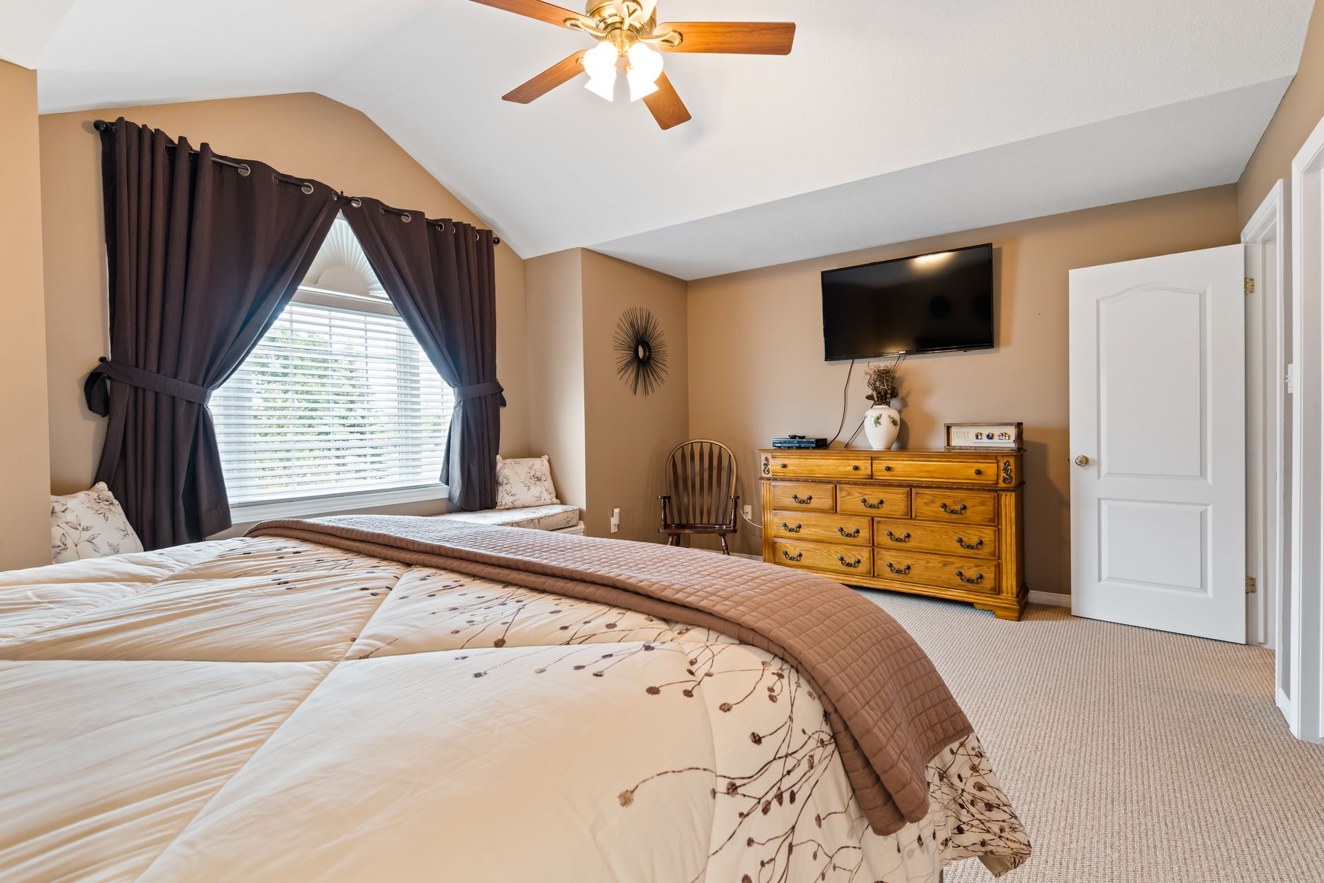 A bedroom with a bed , dresser , television and ceiling fan.