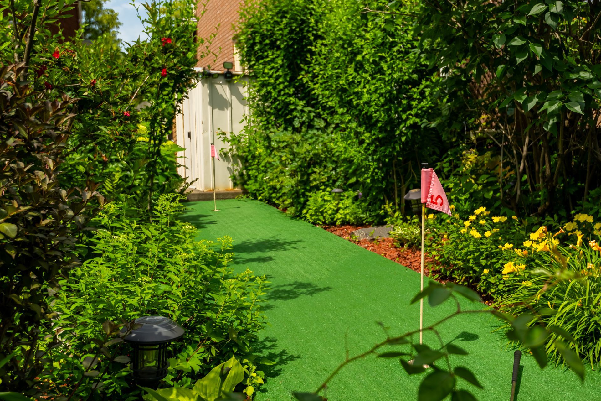 A putting green in a garden with a pink flag