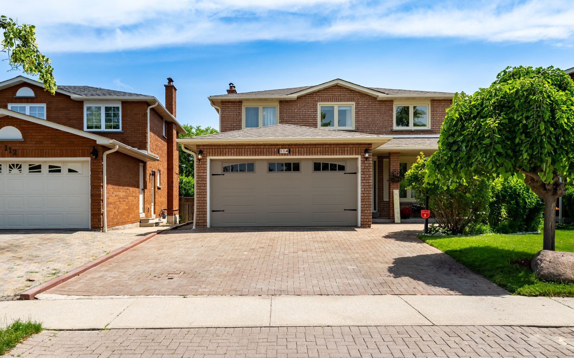 a brick house with two garages and a tree in front of it .