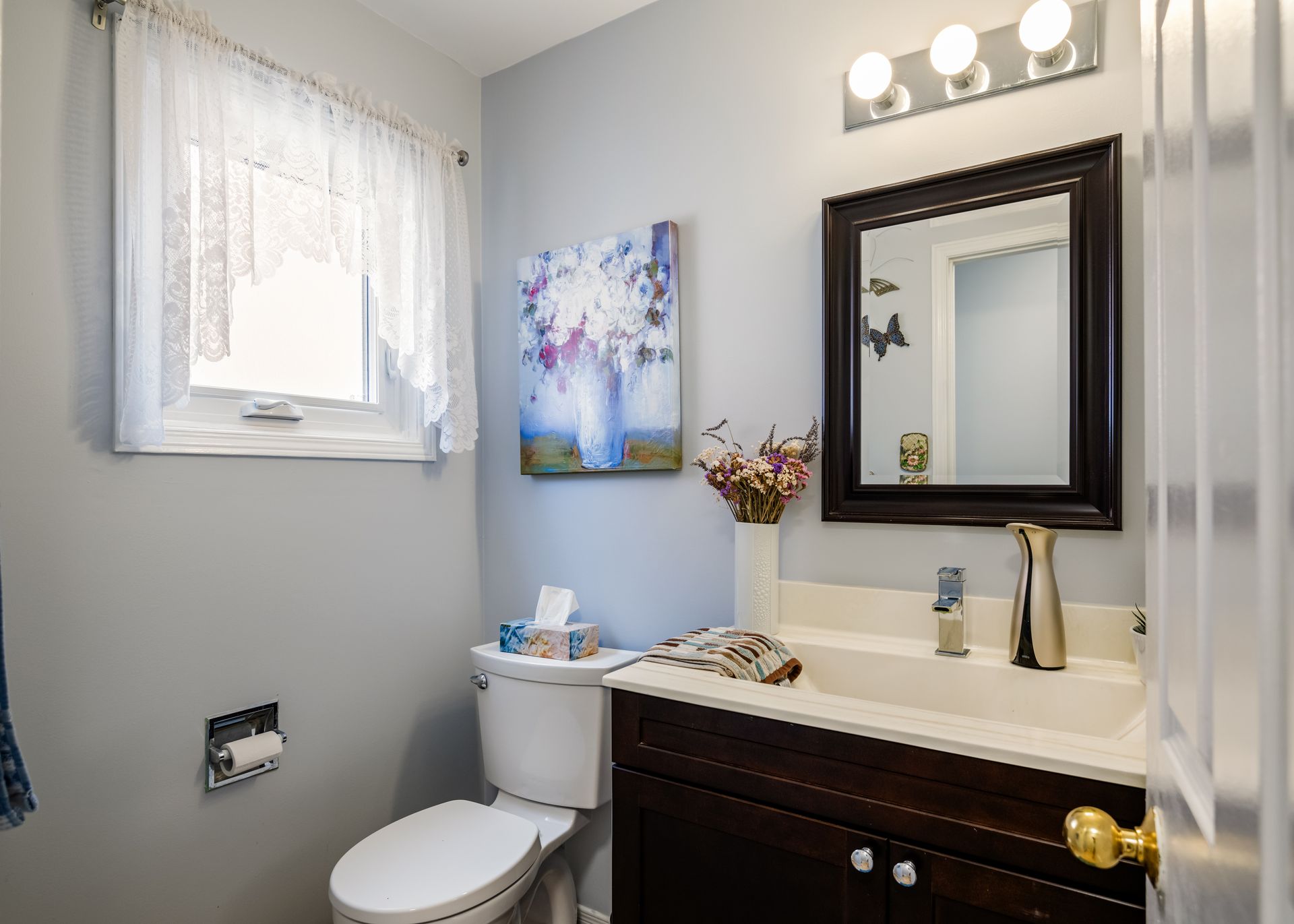 A bathroom with a toilet , sink , mirror and window.