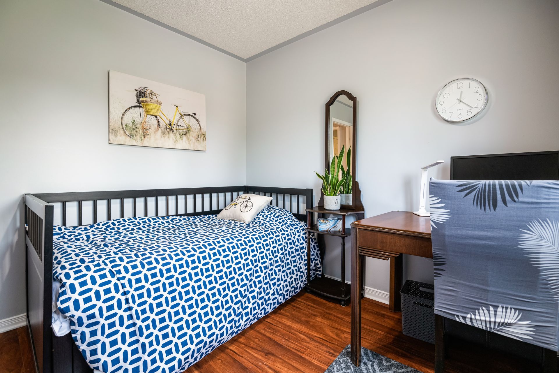 A bedroom with a day bed , desk , chair and a clock on the wall.