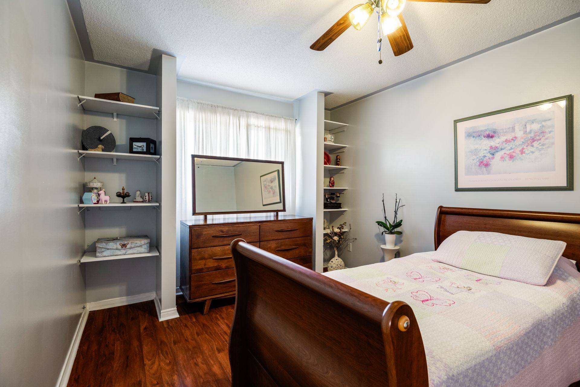 A bedroom with a sleigh bed , dresser , mirror and ceiling fan.