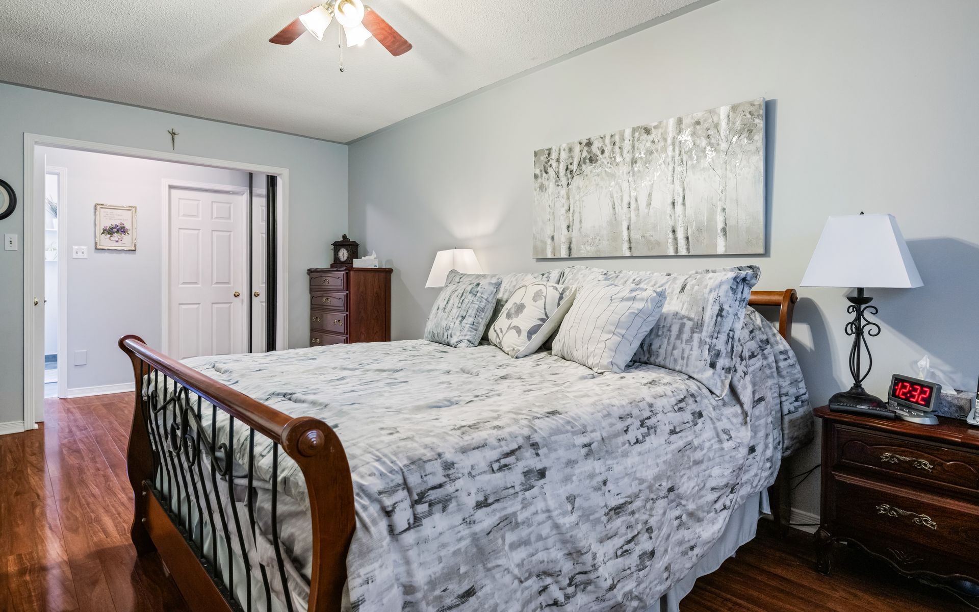 A bedroom with a king size bed , nightstand , lamp and ceiling fan.