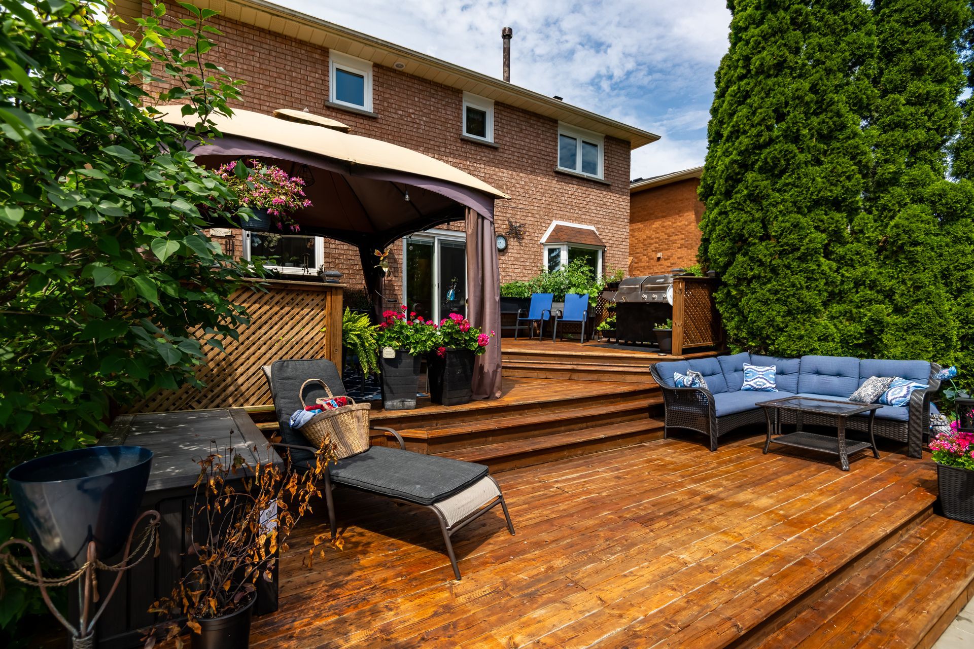 A wooden deck with furniture and a gazebo in the backyard of a house.