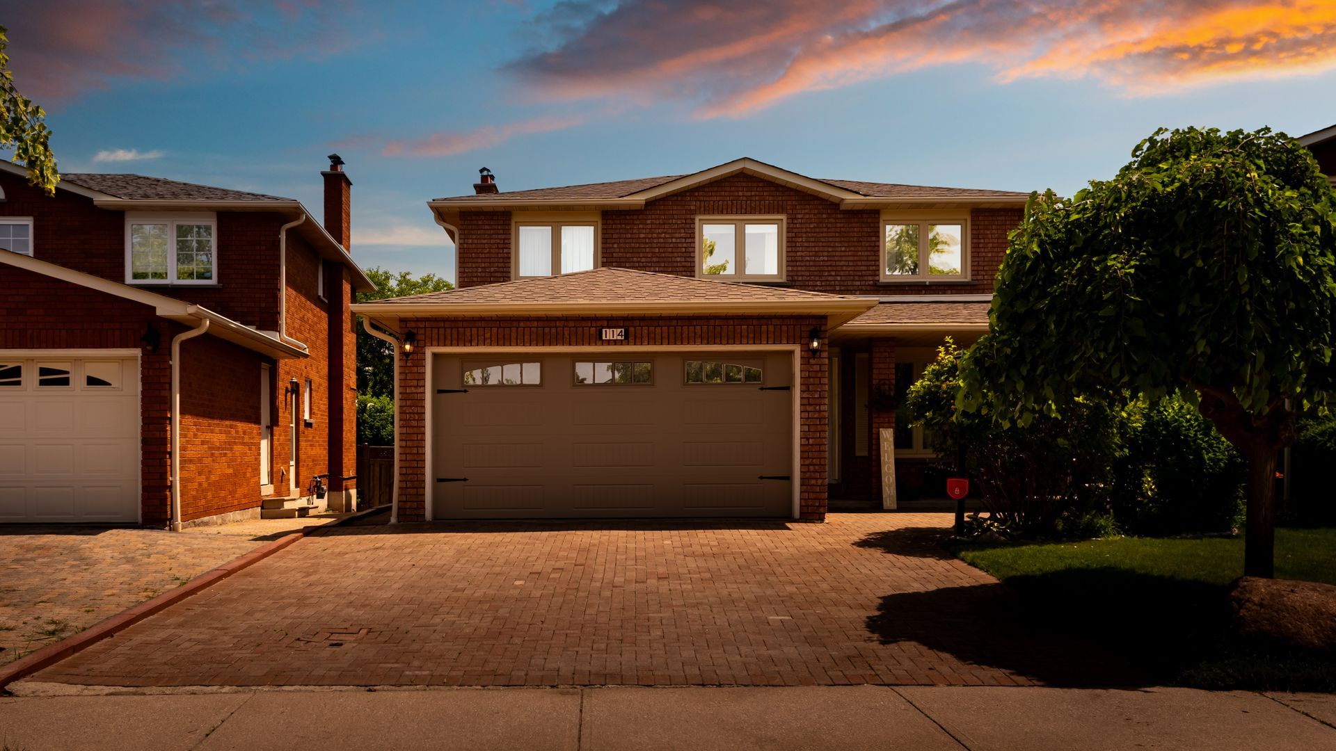 a brick house with two garages and a tree in front of it .