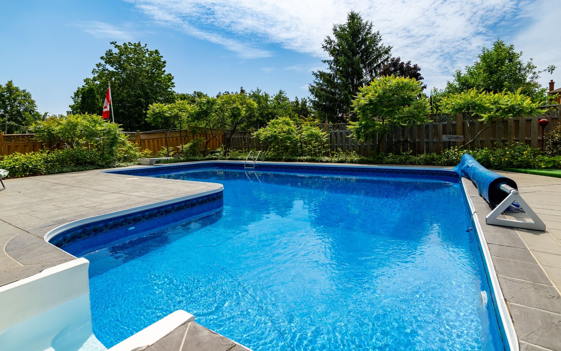 A large swimming pool is surrounded by trees and a fence.