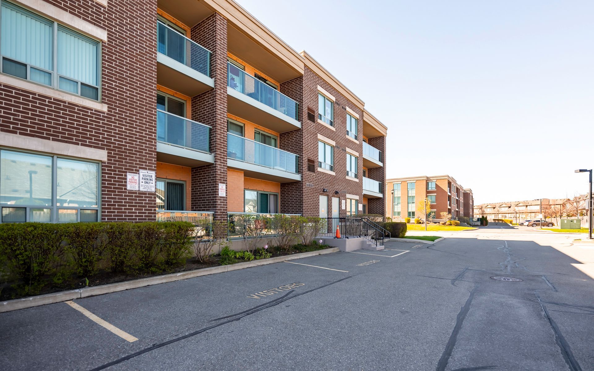 A brick apartment building with balconies and a parking lot in front of it.