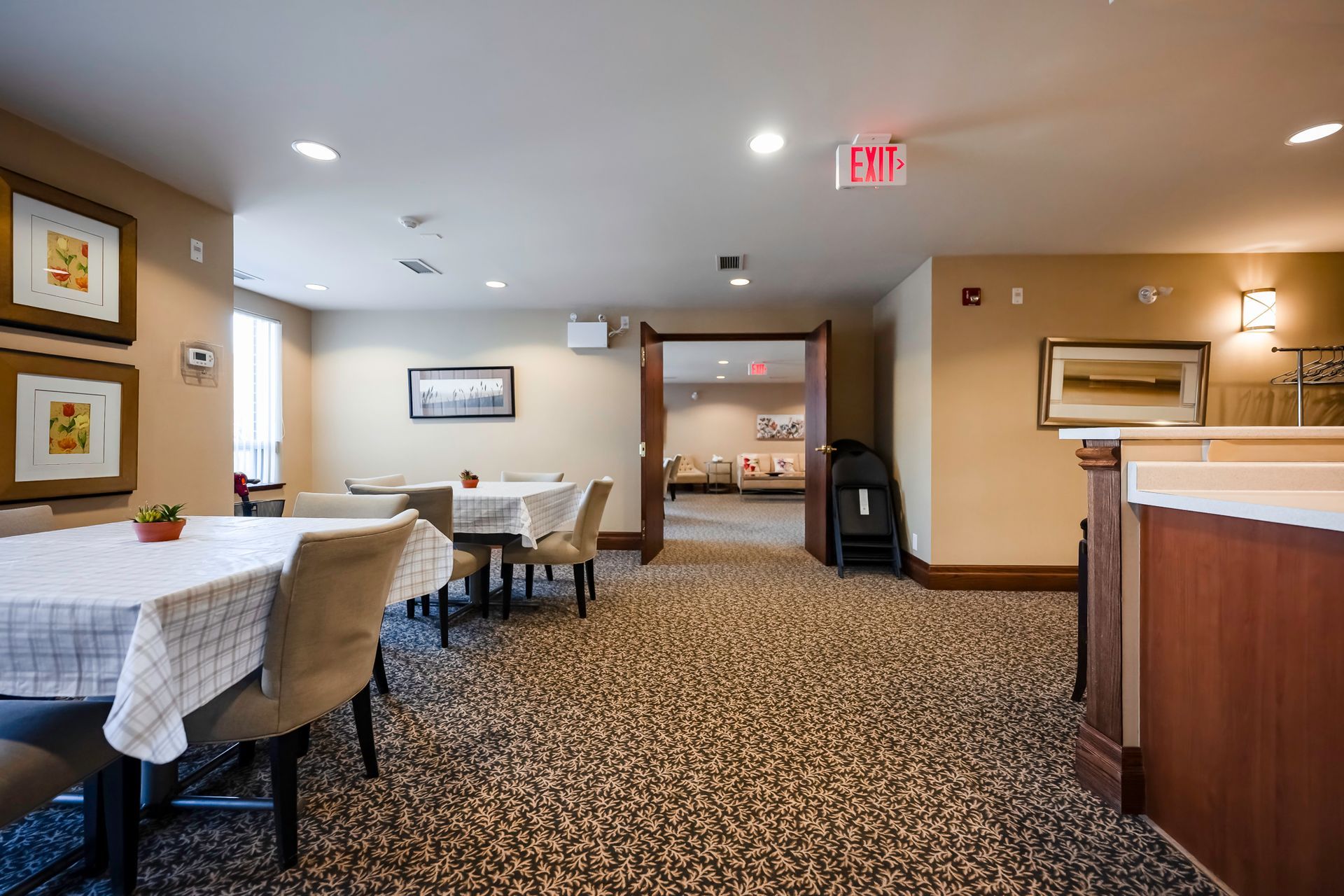 A large room with tables and chairs and a red exit sign.