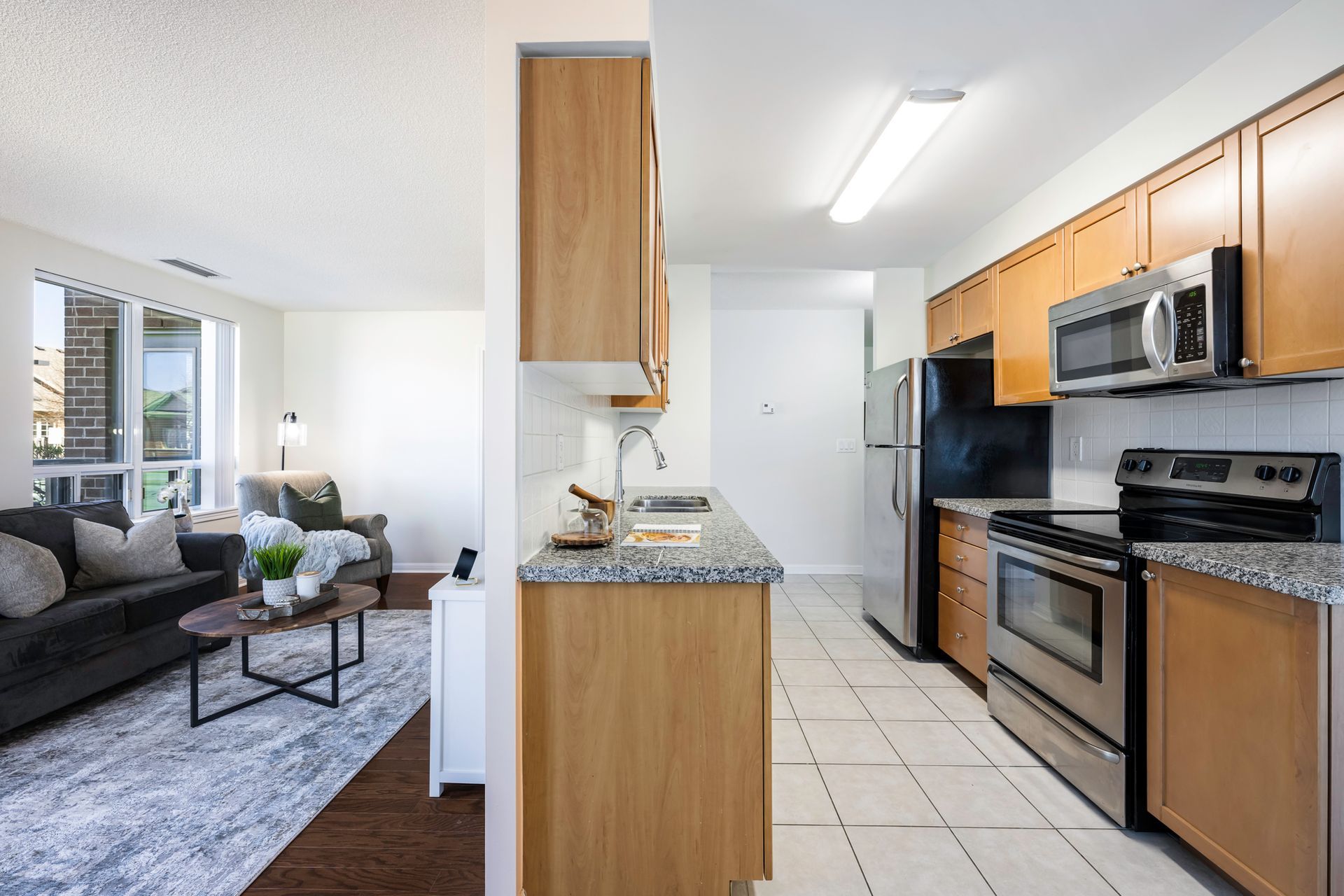 A kitchen with stainless steel appliances and wooden cabinets next to a living room.